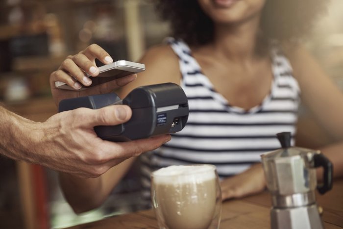 Femme réalisant un paiement mobile sans contact avec un smartphone dans un café, symbole de digitalisation.