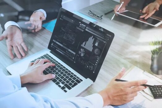 Close-up of business professionals working on laptops and tablets, analyzing data and graphs during a meeting on diversifying an insurance distribution strategy.