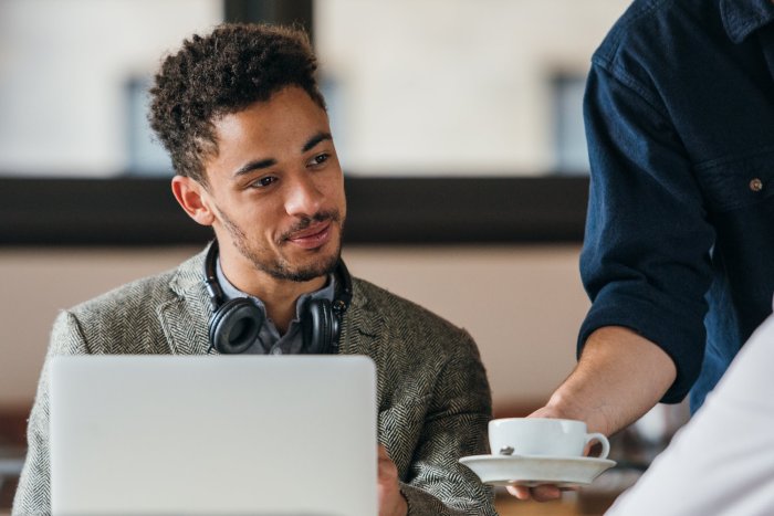 Homme assis devant un ordinateur portable, recevant une tasse de café, illustrant la mise en place d’une stratégie digitale et de community management pour un opérateur mobile.
