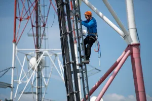 Telecom technician climbing a tower to upgrade a 4G mobile network with advanced features aimed at increasing data speeds.