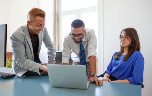 Two men and a woman collaborating around a laptop during a meeting, illustrating the implementation of a fixed number portability solution.