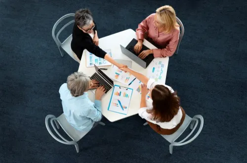 Top-down view of four people in a meeting, shaking hands over charts and laptops, illustrating successful collaboration.