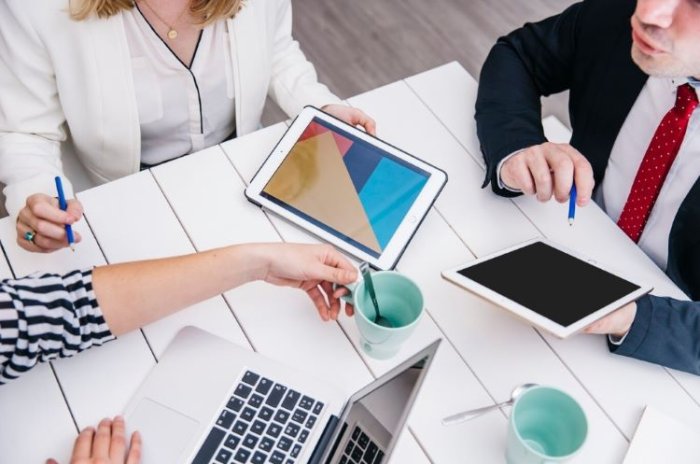 Three professionals in a meeting, discussing a mobile health application using laptops and tablets.
