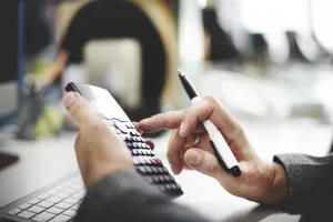 Close-up of a person using a calculator and pen, illustrating the implementation of a standardized BI solution for sales and financial management.