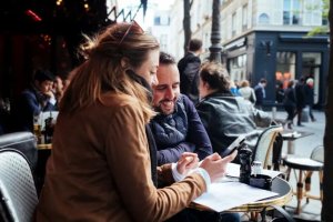 Deux personnes consultant un e-shop sur smartphone à la terrasse d’un café, illustrant l’expérience d’achat multicanale