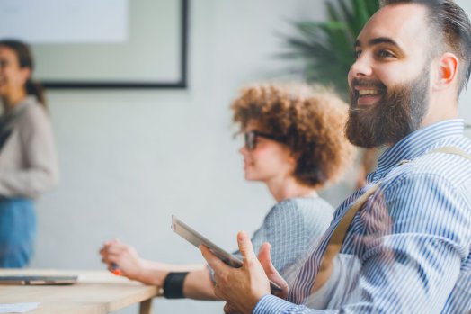 Smiling man holding a tablet during a business meeting, illustrating training on a new B2B CRM.
