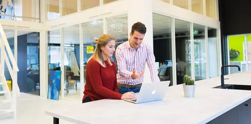 Two colleagues discussing in front of a computer in a modern office, symbolizing Sofrecom's support.