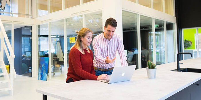 Deux collègues échangent devant un ordinateur dans un bureau moderne, symbolisant l'accompagnement Sofrecom.