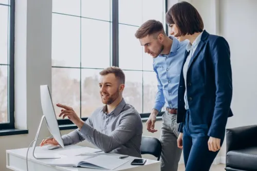 Three professionals reviewing a project on a computer in a modern office, illustrating teamwork and network transformation expertise.