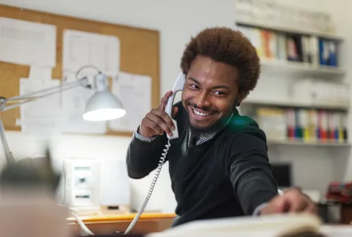 Smiling man on the phone in an office, illustrating the implementation of a centralized OSS/BSS solution for fixed and broadband services.