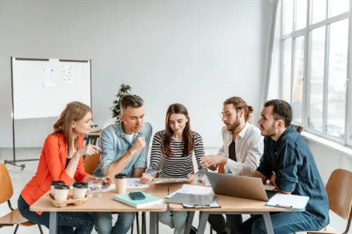Five team members discussing around a laptop and marketing documents, illustrating telecom operators’ strategic thinking on the travel retail market.