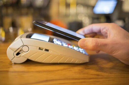 A smartphone making a contactless payment on a POS terminal, illustrating the rise of digital financial services in emerging markets.